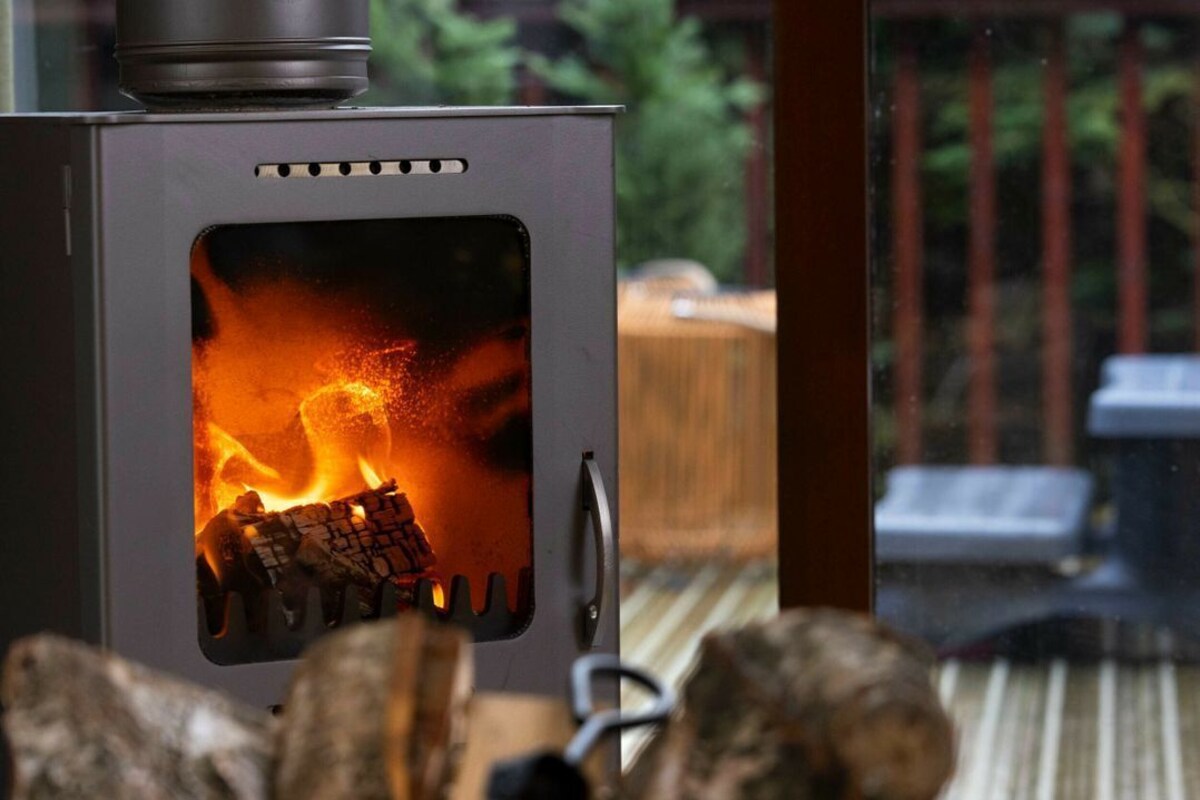 A wood-burning stove with logs burning inside, set on a wooden deck.