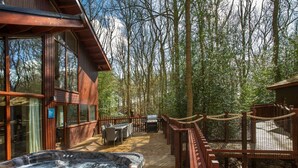 A wooden deck with a hot tub, outdoor furniture, and a barbecue area surrounded by trees. - Blackwood Forest - Forest Holidays (Winchester)