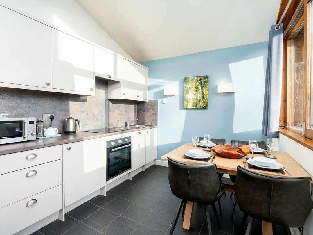 Una cocina moderna con armarios blancos, una mesa de comedor para dos personas y un ventanal con vistas a árboles.