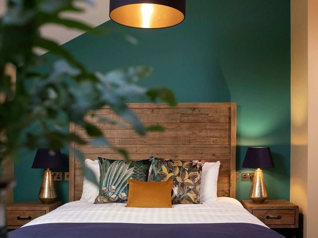 Un dormitorio con cabecera de madera, cama con almohadas estampadas, dos lámparas de noche y una lámpara colgante.
