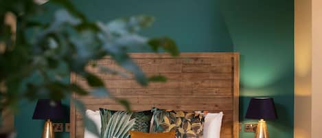 A bedroom with a wooden headboard, a bed with patterned pillows, two bedside lamps, and a hanging light fixture.