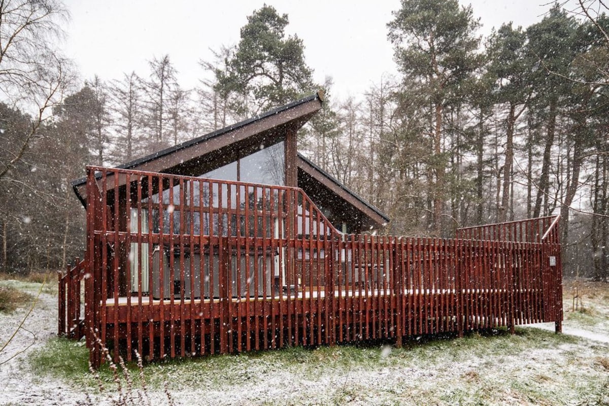 A cabin with a sloped roof, a wooden deck, and a fenced area.