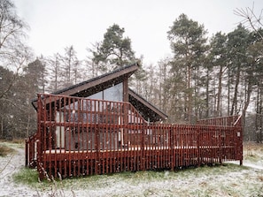 A cabin with a sloped roof, a wooden deck, and a fenced area.