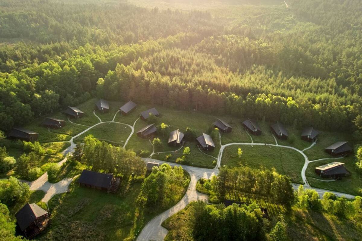 Vista aérea de uma área arborizada com várias cabanas dispostas em semicírculo, ligadas por caminhos sinuosos.