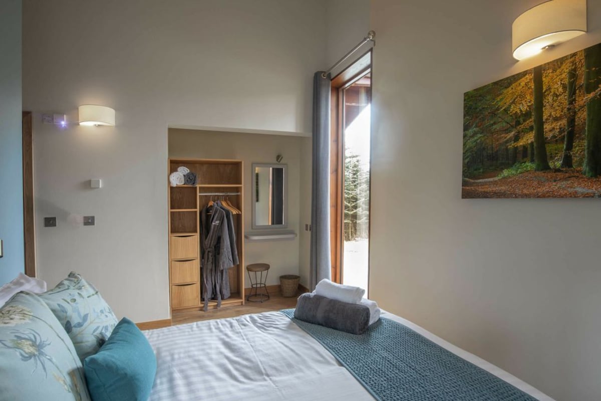 A bedroom with a bed, a wardrobe, a mirror, a window, and a painting.