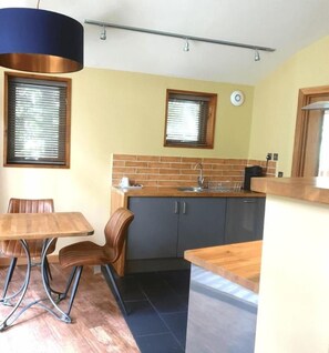 A compact kitchen with a dining area, a sink, and a window with blinds. - Cropton Forest - Forest Holidays (Pickering)