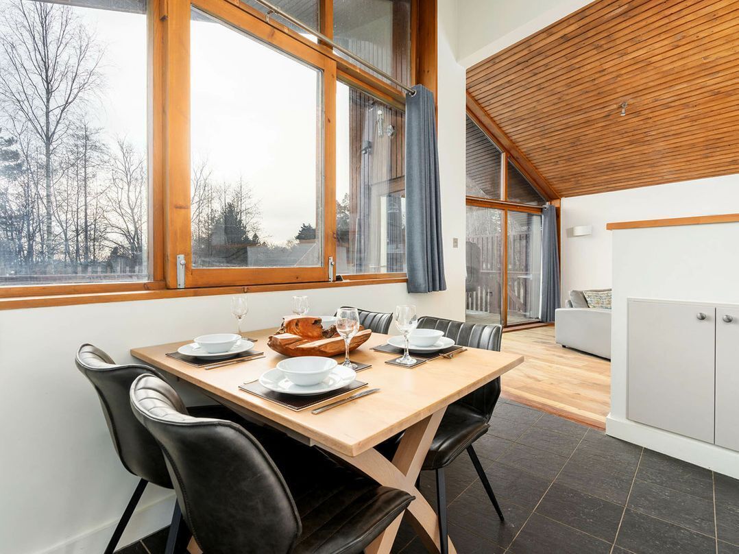 Un comedor con una mesa de madera, sillas negras y vistas al exterior a través de amplios ventanales.