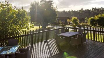 An outdoor deck with a table and chairs, surrounded by a wooden fence, overlooking a grassy area with trees.