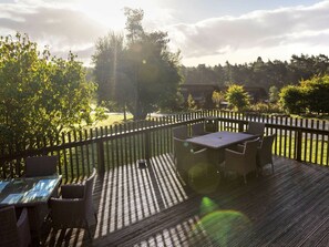 An outdoor deck with a table and chairs, surrounded by a wooden fence, overlooking a grassy area with trees. - Cropton Golden Oak (Pickering)