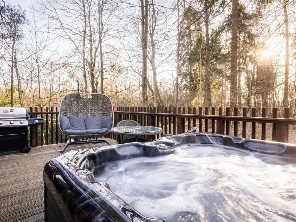 A hot tub on a wooden deck with a grill and a chair.