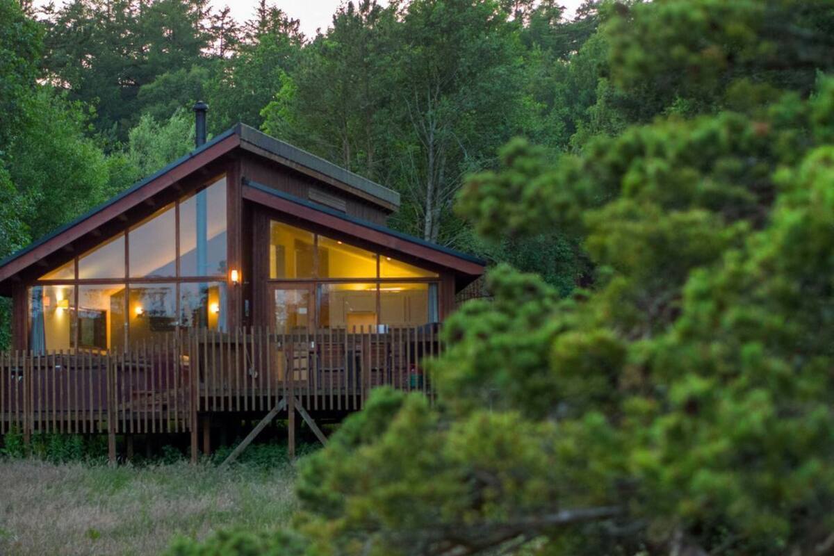A cabin with a wooden deck, large windows, and a chimney.