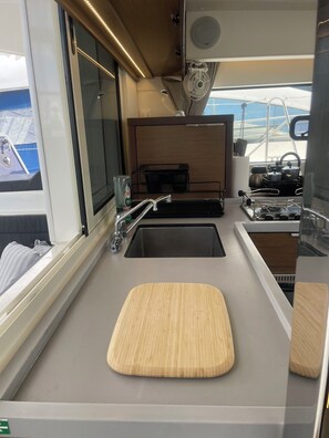 A compact kitchen with a sink, a cutting board, and a stove. - Sun-Kissed Sailing Adventure in Islas Sarónicas (Alimos)