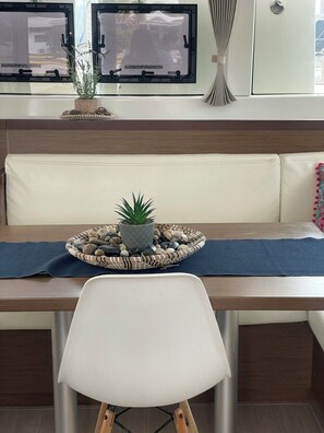 A modern kitchen with a built-in bench, a dining table, a white chair, and a potted plant. - Sun-Kissed Sailing Adventure in Islas Sarónicas (Alimos)