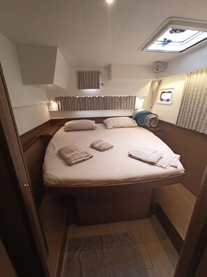 Ein kompakter, gut beleuchteter Schlafraum mit Dachfenster, einem Bett mit ordentlich drapierten Handtüchern und einem kleinen Fenster.