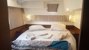 A hotel room with a bed, pillows, a quilted blanket, and a towel rack with towels. - Sun-Kissed Sailing Adventure in Islas Sarónicas (Alimos)