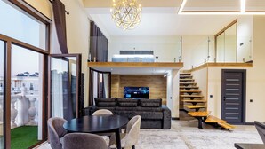 A modern living area with a sofa, dining table, and chairs, a staircase, and a television.