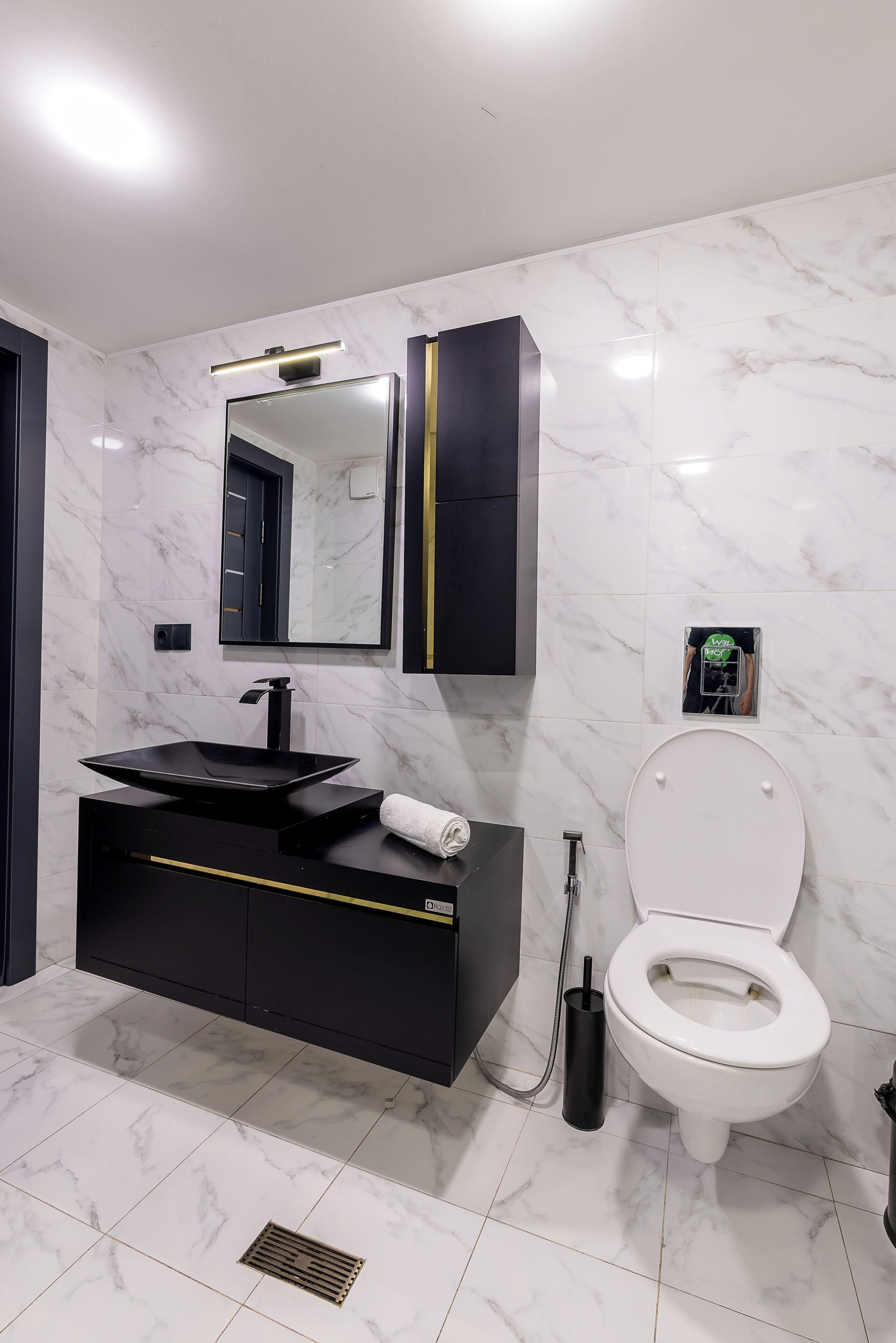 Une salle de bain moderne avec un meuble-lavabo noir, des toilettes blanches et un sol carrelé en marbre.