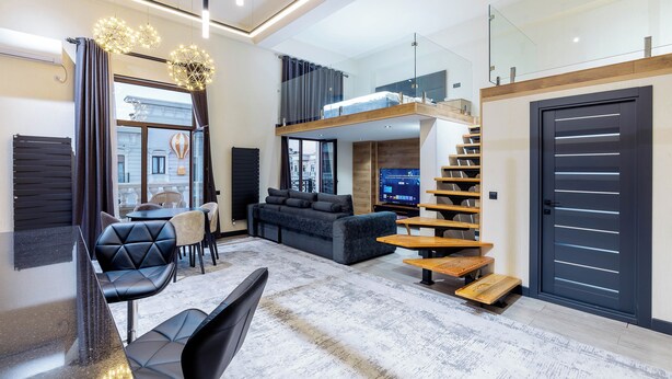A modern living room with a sofa, chairs, a coffee table, a staircase, and a TV.