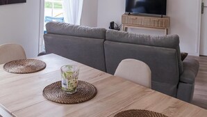 Ein modernes Wohnzimmer mit einer Couch, einem Fernseher und einem Esstisch mit Platzsets.