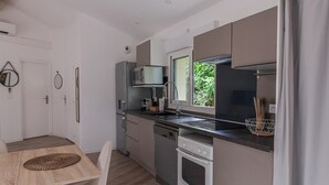 Eine moderne Küche mit Mikrowelle, Backofen und Spüle. Ein Esstisch mit Stühlen und ein Fenster mit Blick auf Grünflächen.