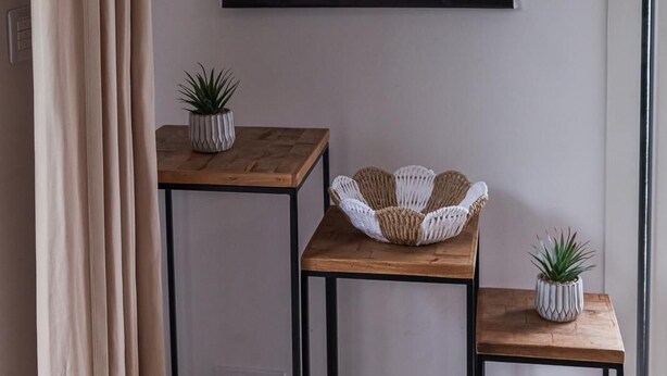 Ein Zimmer mit einem großen gerahmten Kunstwerk an der Wand, zwei kleinen Tischen mit Blumentöpfen und einem gewebten Korb auf einem Tisch.