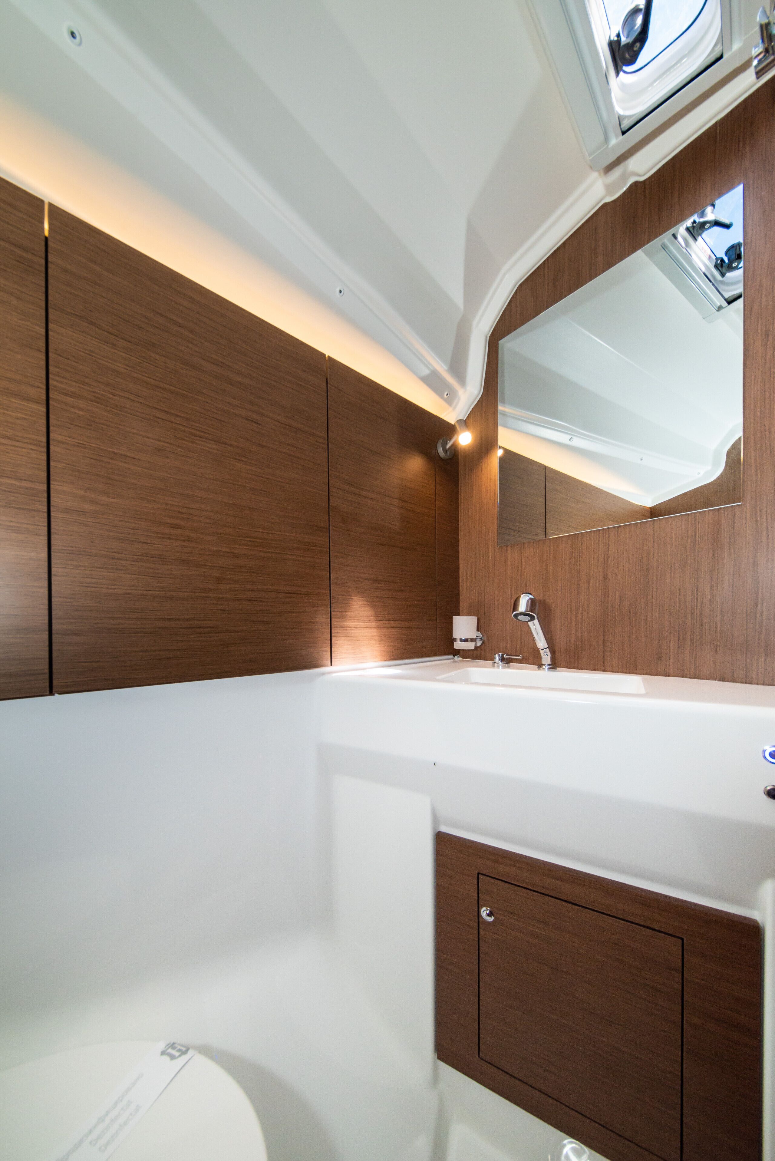 A modern bathroom with a large mirror, a white sink, and wooden cabinetry.