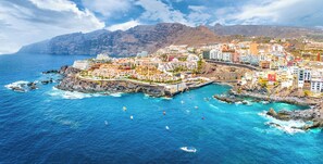 A coastal town with buildings along the shoreline, a bridge connecting the land, and boats in the water.