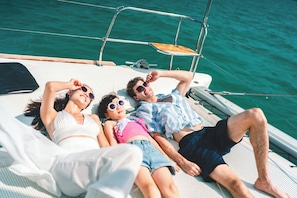 A boat with a metal railing, a wooden seat, and a person lying on a mat.
