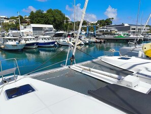 Un puerto deportivo con varias embarcaciones amarradas, cielo despejado y edificios al fondo.