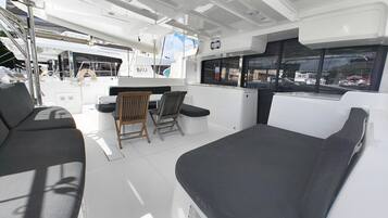 Interior de un barco con asientos, una mesa y vista al puerto deportivo.