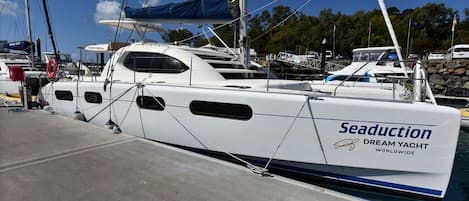 A white yacht named 'Seaduction' docked at a marina with other boats and a clear sky.