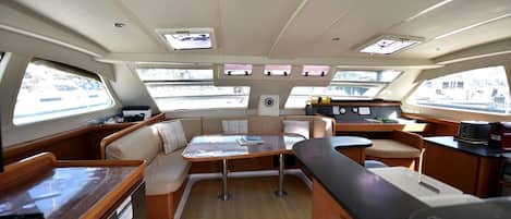 A boat interior with a dining area, seating, and a control station.