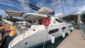 Un yate blanco amarrado en un puerto deportivo, con un flotador salvavidas, una cubierta sombreada y cielo despejado.
