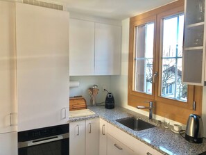 A kitchen with white cabinets, a granite countertop, a stainless steel sink, and a window with a view of trees. - Oberland Nr. 29 Appartement/Fewo, Dusche oder Bad, WC 6-Bettwohnung by Interhome (Gstaad)