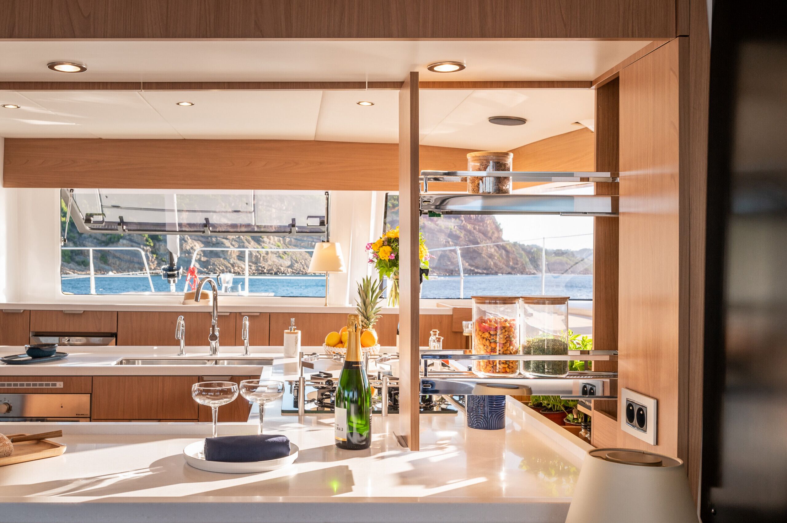 A modern kitchen with a large window, wooden cabinets, and a view of the sea.