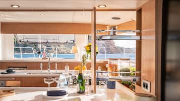 A modern kitchen with a large window, wooden cabinets, and a view of the sea.