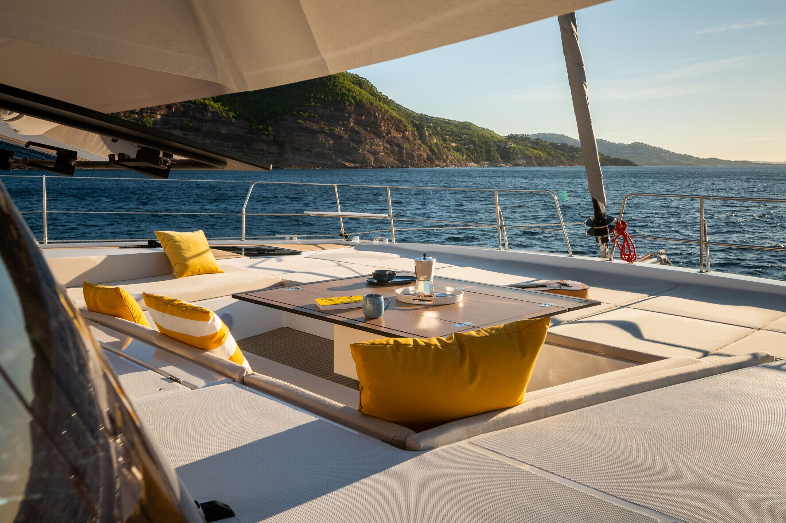 Le pont d’un yacht, avec des sièges, une table et une vue sur la mer et les falaises.
