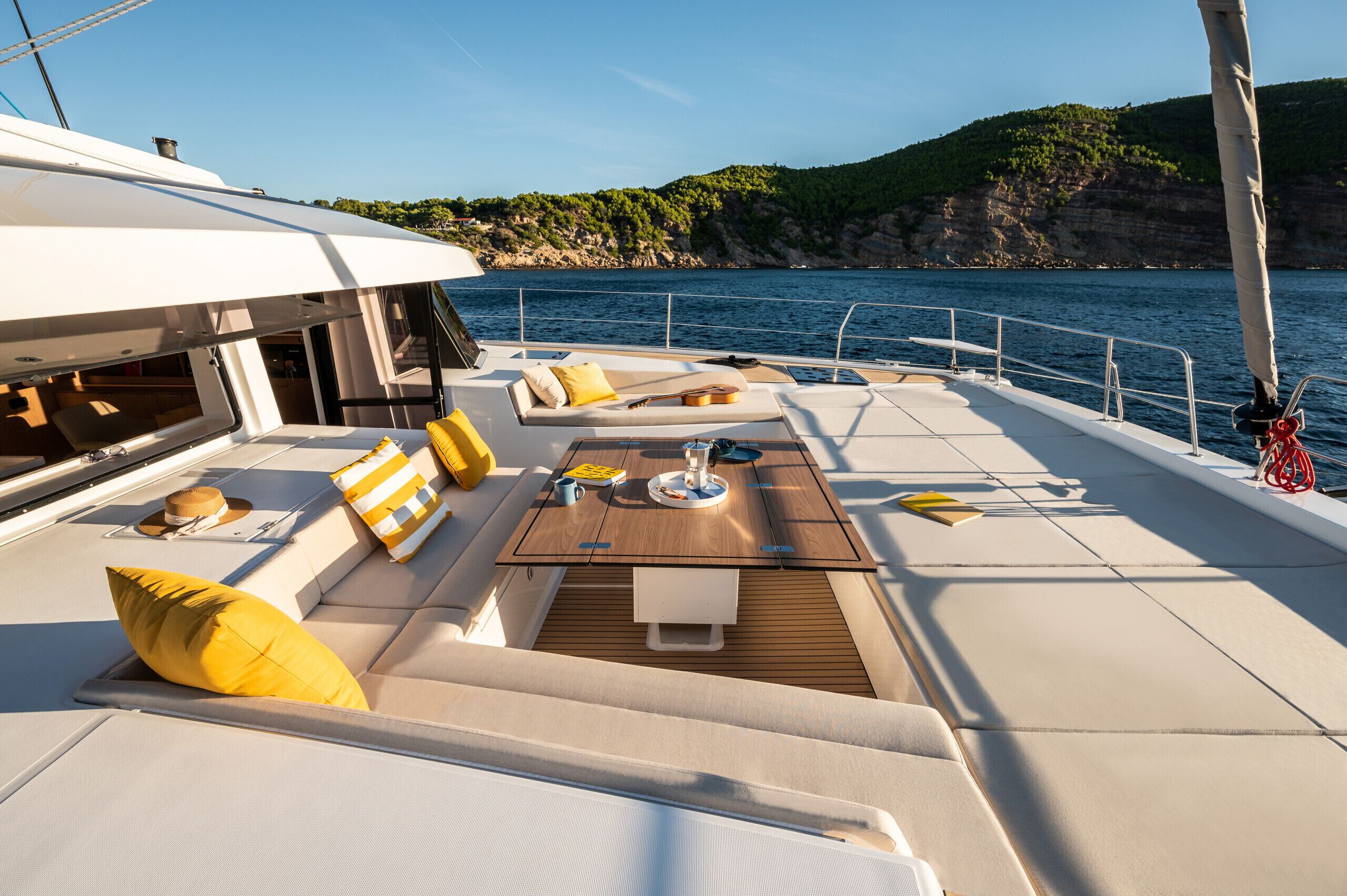 A yacht deck with seating, a table, and a view of the sea and cliffs.