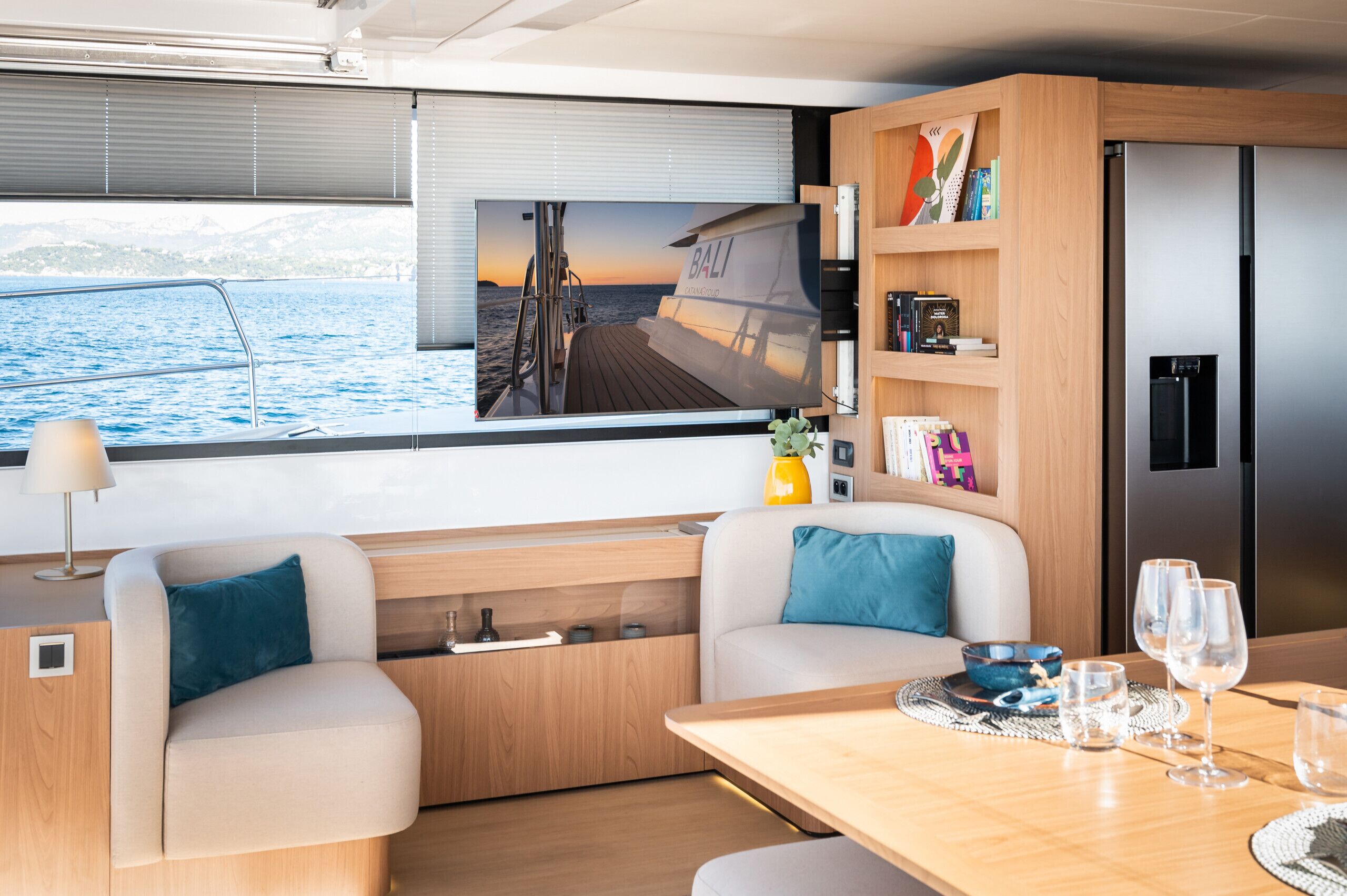 A modern interior with a TV displaying a scenic view, a dining area with a table set for two, and a kitchen area with a refrigerator.