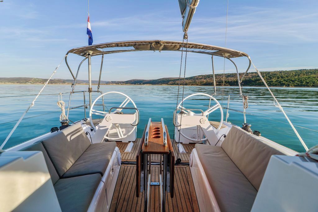 A boat's deck with two steering wheels, a canopy, and a view of calm water and distant land.