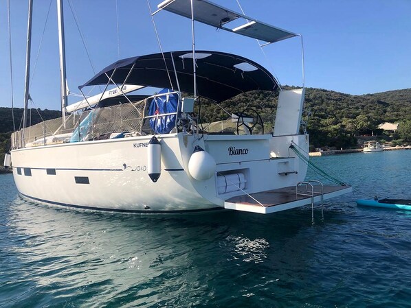 A sailboat with a covered deck, a name 'Bianco' on the side, and a small boat docked at the stern.