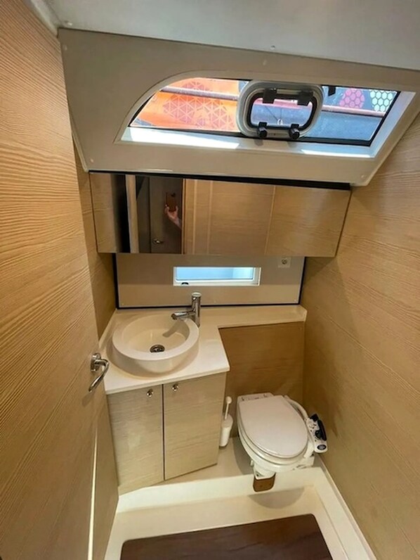A compact bathroom with a toilet, sink, and a small window above the sink.
