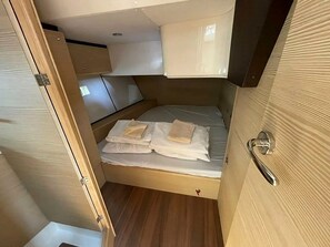A compact sleeping area with a bed, a small shelf, and a door.