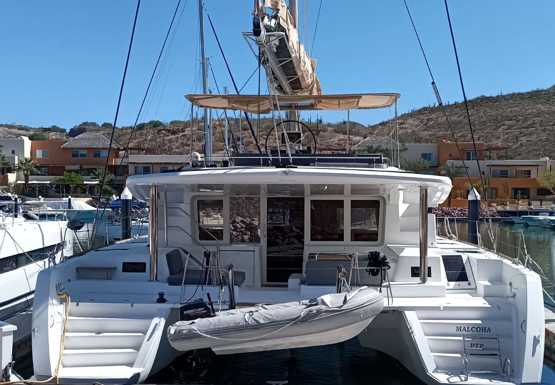 Um iate branco atracado em um porto, com área de cabine, deck coberto e vista para o porto e edifícios ao fundo.