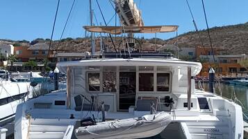 Eine weiße Yacht liegt in einer Marina vor Anker, mit einer Kabine, einem überdachten Deck und Blick auf die Marina sowie Gebäude im Hintergrund.