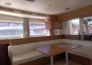 A compact boat interior with a cushioned seating area, a small table, and windows providing views of the outside.