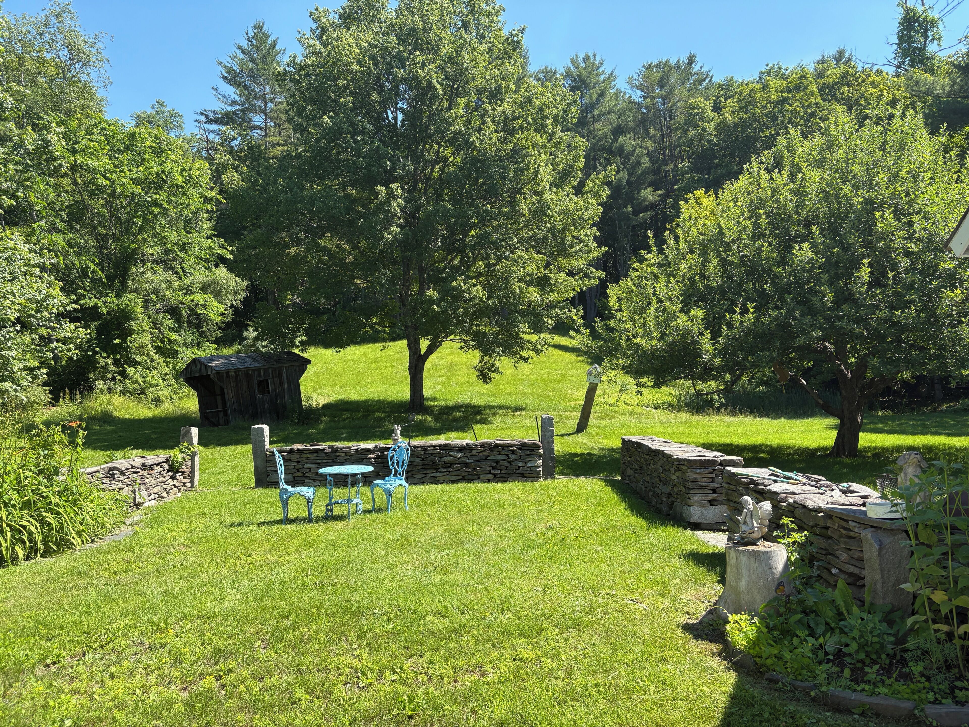A rustic outdoor setting with a stone wall, a small wooden structure, and a blue metal table and chair set.