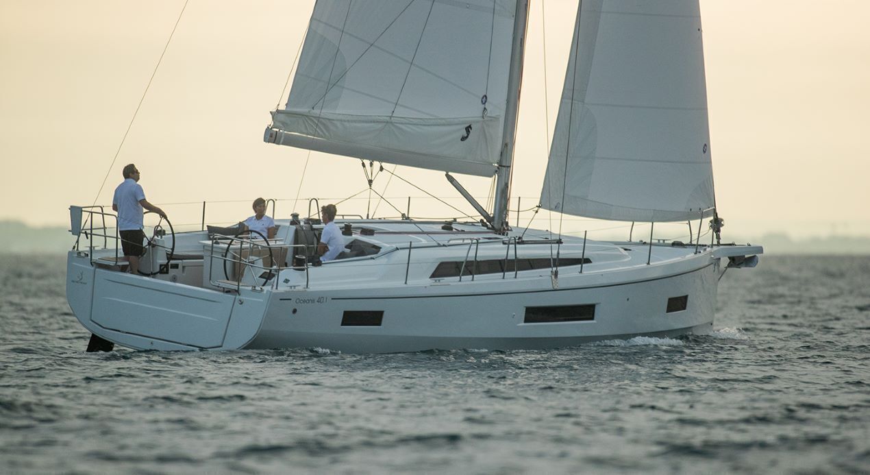 Een zeilboot met twee personen aan dek, één aan het roer en één zittend.