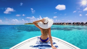 Eine Person auf einem Boot mit freiem Blick auf türkisfarbenes Wasser und Overwater Bungalows im Hintergrund.