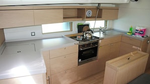 A compact kitchen with a stove, oven, and sink. There is a window above the sink, and a small bench to the right. - Dubrovnik Delight: A Sun-Kissed Sailing Experience (Komolac)